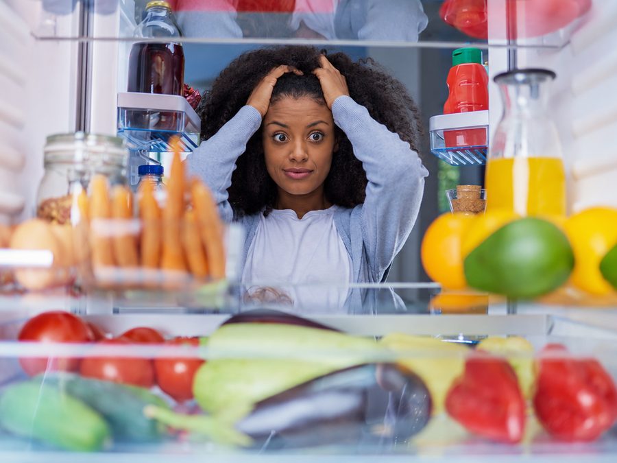 Woman looking confused and overwhelmed inside an open fridge full of food