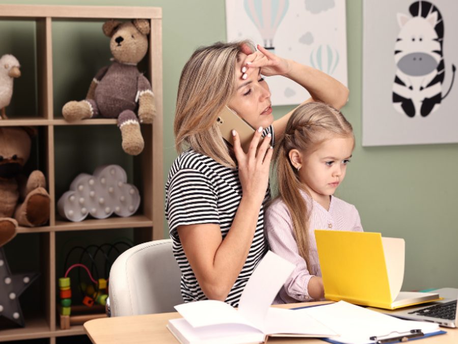 Stressed mother on the phone while working at a desk beside her young daughter